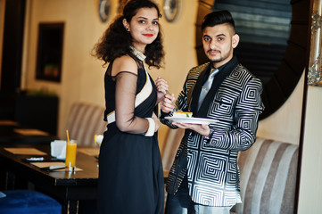 Lovely indian couple in love, wear at saree and elegant suit, posed on restaurant, hold plate with cake.