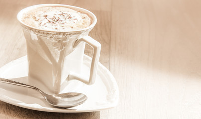 Chocolate flakes and milk froth - cup of cappuccino coffee on vintage wooden table