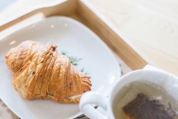 Croissant with salmon and green grass and tea on the wooden table.