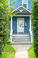 Main entrance of old family house with doorsteps and pathway through green hedgerow fence