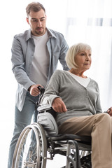 bearded man carrying disabled mother on wheelchair at home