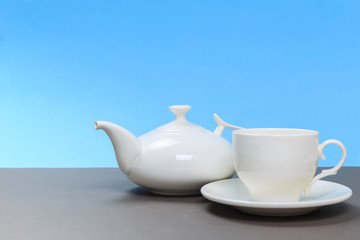 vintage white porcelain teapot and cup on gray board and blue background