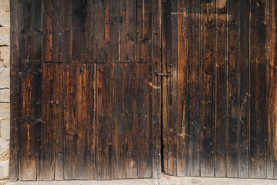 Very old wooden door of a warehouse or a barn. Big old gate made of wood. Dark wooden planks on a rural barn gate. Wooden texture or background.