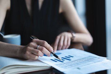 Accountant woman checking paperwork while sitting near window in creative office or cafe. Confident young woman working with documents.