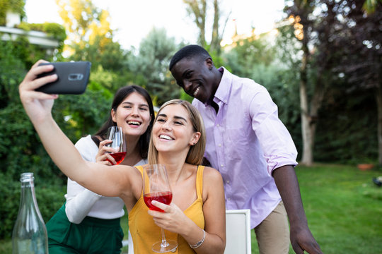 Friends having fun at a summer dinner in the garden, taking selfies