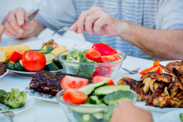 people sitting at table and eating grilled chicken wings and vegatebles