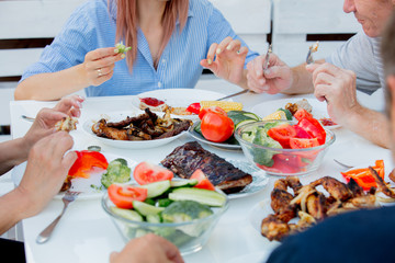 people sitting at table and eating grilled chicken wings and vegatebles