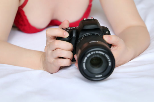 Hot woman in red bra lying with DLSR camera in the bed. Concept of adult movies and photography, erotic shooting, girl photographer, sexy lingerie