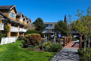 Residential District in Richmond City, a village of townhouses with pond and fountain, blossom of sakura, green grass bushes and trees in the territory of residential complex, Vanсouver, British Colum