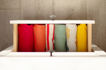 Children's clothing in bright colors is folded in a neat row in a drawer against the gray wooden floor