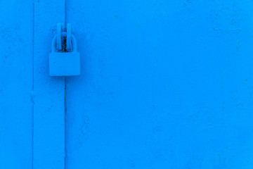Background of old metal doors with a padlock painted in blue close up