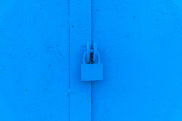 Background of old metal doors with a padlock painted in blue close up