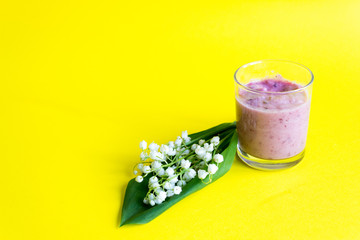 Obraz na płótnie Canvas Fresh berry smoothie on a yellow background. Lilies of the valley and smoothies of berries. Spring concept