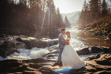 Amazing wedding couple, bride and groom holding hands on a mountains and rivers background. Cute...