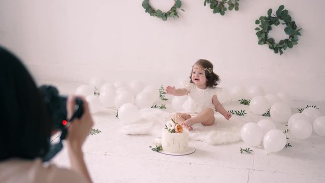 Female photographer takes pictures of little girl in decorated photo studio.