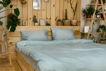 Real photo of a botanical bedroom interior with wooden shelves,  double bed and plants. Bedroom wooden interior with plants next to a bed made with pillows.