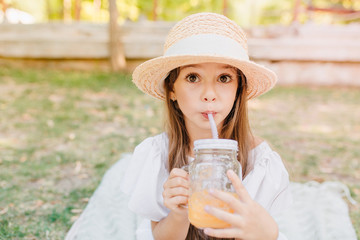 Surprised girl with brown eyes drinking tasty juice in hot summer day. Outdoor portrait of cute...