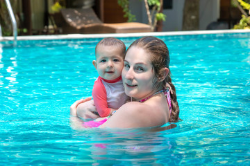 Naklejka premium Happy mother with little baby daughter swims in the pool at summer holiday. Sunny day. Tropics. Infant watching to camera