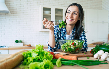 Healthy lifestyle. Good life. Organic food. Vegetables. Close up portrait of happy cute beautiful young woman while she try tasty vegan salad in the kitchen at home. - obrazy, fototapety, plakaty