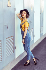 young woman in blue denim overalls and yellow tshirt with black hat sensual looking at camera while...