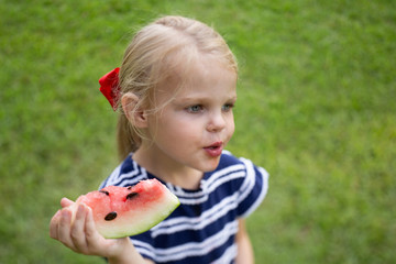 Blonde haired blue eyed 4 year old girl eating watermelon in summer