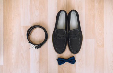Wedding details, morning groom. Leather shoes, bow tie and belt lie on the background of beige parquet. Composition and concept.