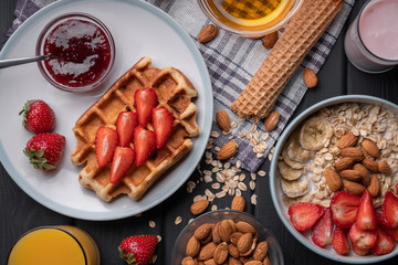Morning meal set. Breakfast. Delicious oatmeal granola with berries, nuts and honey. A crispy waffle topped with strawberry jam. On a black table background. Top view