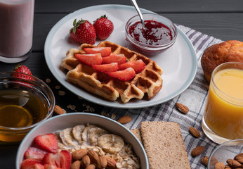 Breakfast. Oatmeal. Muesli. Snack. Sweet waffles. Morning fresh food. Berry, almond, jam, juice. Dessert on black table background. Closeup