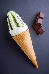 Ice cream cone and chocolate on a slate board. Waffle cone with ice cream on slate board. Dessert with jam on black background. Flat lay