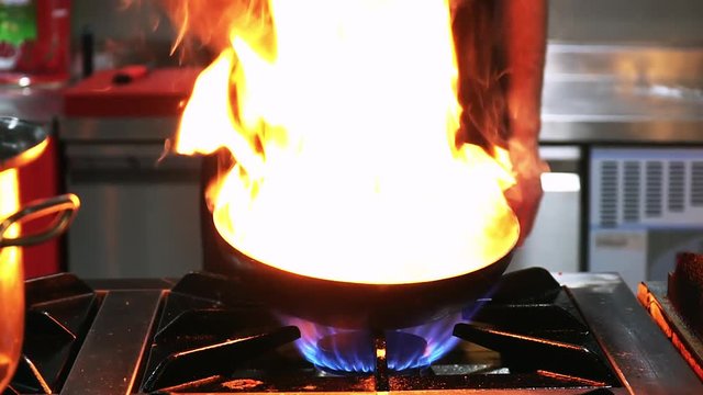 Close-up view of a chef cooking flambe style dish on a pan in restaurant kitchen.