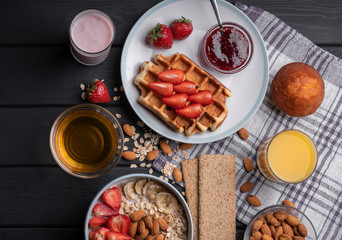 Breakfast. Oatmeal. Muesli. Snack. Sweet waffles. Morning fresh food. Berry, almond, jam, juice. Dessert on black table background. Closeup