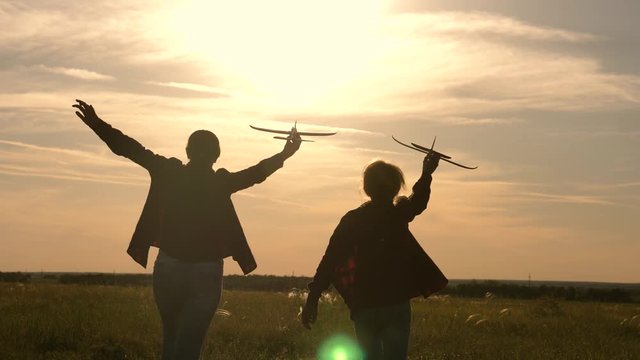 Children are bugger on background of sun with an airplane in hand. Two girls play with a toy plane at sunset. Silhouette of children playing on plane. Dreams of flying. The concept of children's games