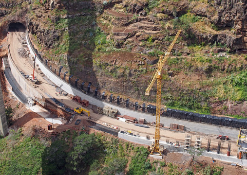 aerial view of a new road under construction with crane and construction materials and machinery working on the site with a tunnel being excavated through the landscape in funchal madeira
