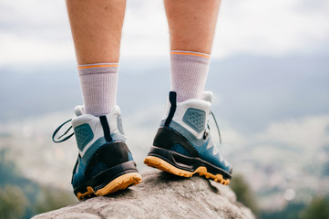 Mood photo of male legs wearing sportive hiking shoes with strong protective sole. Mens legs in trekking footwear for mountain travel standing on stone outdoor at nature on abstract background.