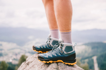 Mood photo of male legs wearing sportive hiking shoes with strong protective sole. Mens legs in trekking footwear for mountain travel standing on stone outdoor at nature on abstract background.