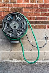 Watering hose reel secured by holder against brick wall