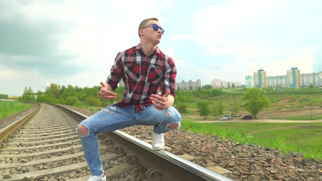The guy walks on rails and sings a song, rap. A music video is shot, the guy reads rap, goes by rail, against the backdrop of the city on an elevated hill. Summer, sunny day.