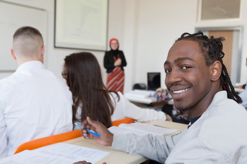 African american male student smiling into camera during class. Female muslim professor explain lesson to students and interact with them in the classroom.Helping a students during class.