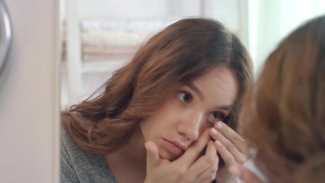 Young woman putting contact lens for eye front bathroom mirror in home