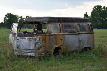 A classic Bus sits abandoned in the middle of a grassy, southern field.