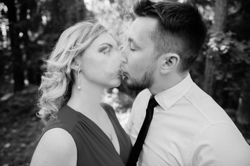 Odd excited happy loving couple outdoor summer portrait. Male vape smoker blowing thick cloud of smoke while kissing his charming girlfriend in dress with red lisptick on her lips. Smoking addiction
