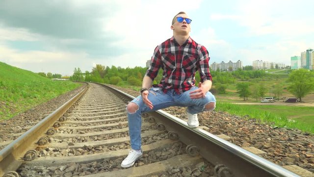 The guy walks on rails and sings a song, rap. A music video is shot, the guy reads rap, goes by rail, against the backdrop of the city on an elevated hill. Summer, sunny day.
