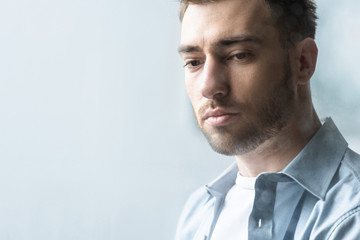 pensive bearded man in blue shirt looking down at home