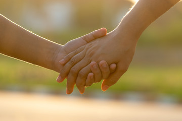 Close up of mother and a child hands at the sunset with copy space. Love concept or family concept.