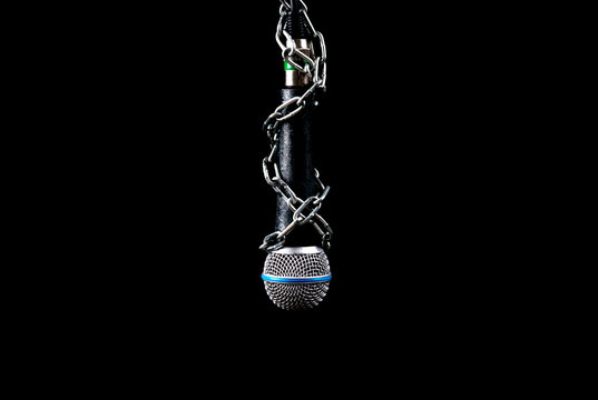 Microphone with a chain, depicting the idea of freedom of the press or freedom of expression on dark background. World press freedom day concept. Using space for advertiser or background.
