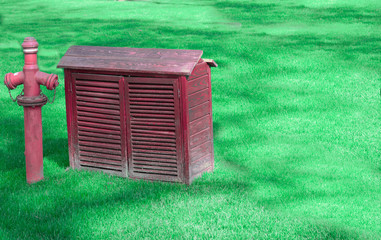 Small hut beside fire hydrant. On the grass. Hut with fire hydrant in red color.