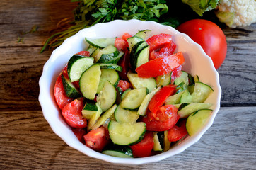 Vegetable salad from cucumbers and tomatoes on a wooden background, rustic table.