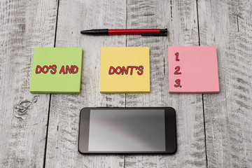 Writing note showing Do S Is And Dont S Is. Business concept for advising Rules or customs concerning some activity Stationary equipment and phone with paper sheets on the wooden desk