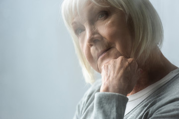selective focus of pensive senior woman with grey hair propping face with hand