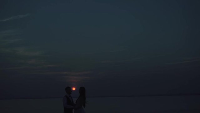 loving couple - young groom and beautiful bride at sunset , silhouette view. They are holding hads
